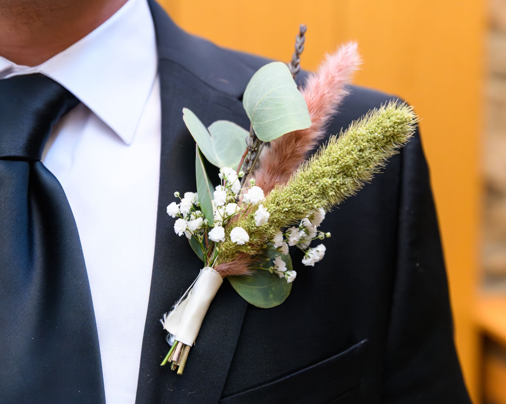 A boutonniere of white baby&rsquo;s breath, eucalyptus, and dried grasses on a dark suit jacket