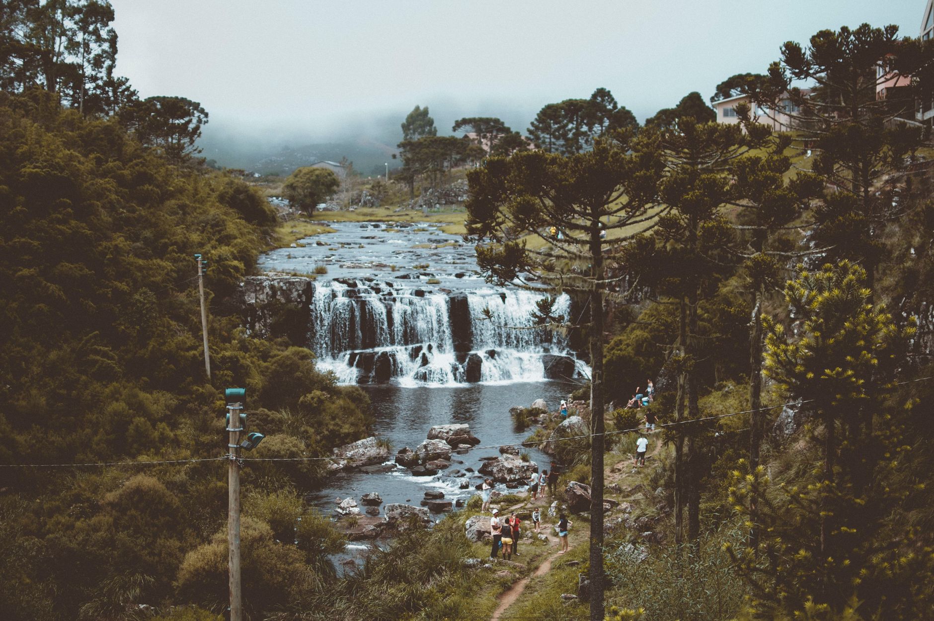 A waterfall below a forested hillside with a few visitors standing on the rocks