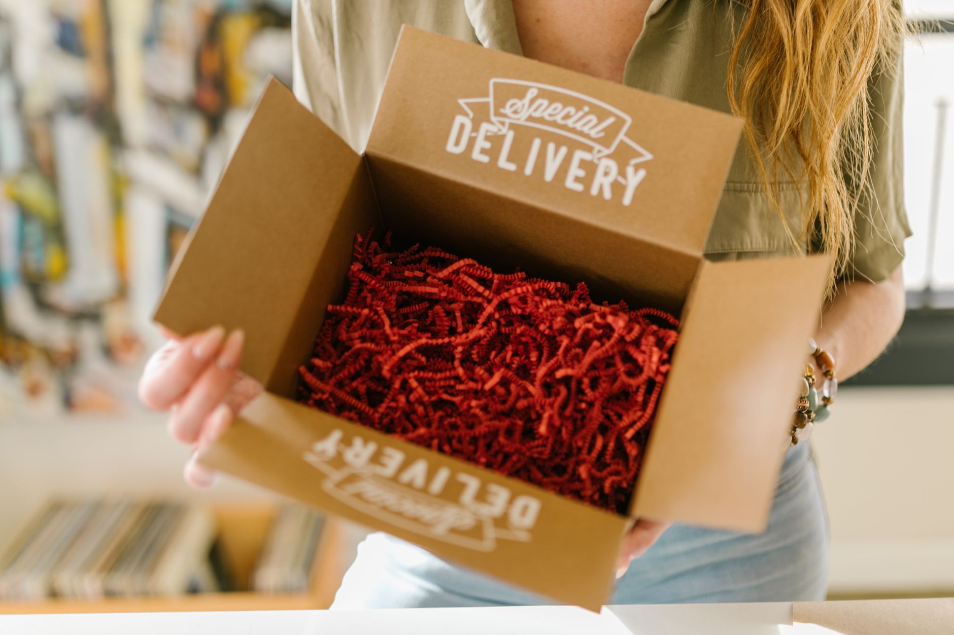 A person opening a cardboard box filled with red paper shred