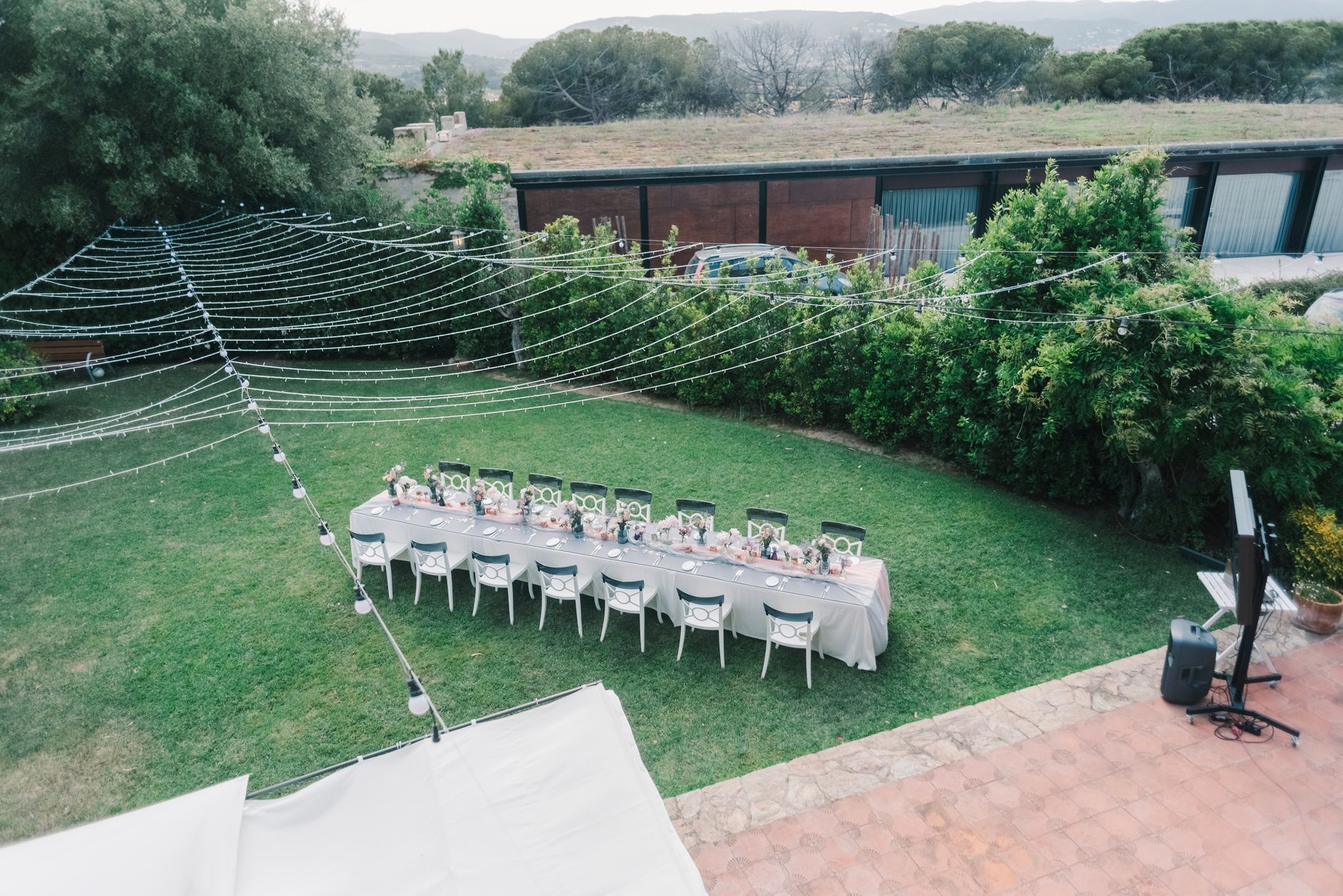 An aerial view of a long outdoor dinner table beneath rows of string lights on a lawn