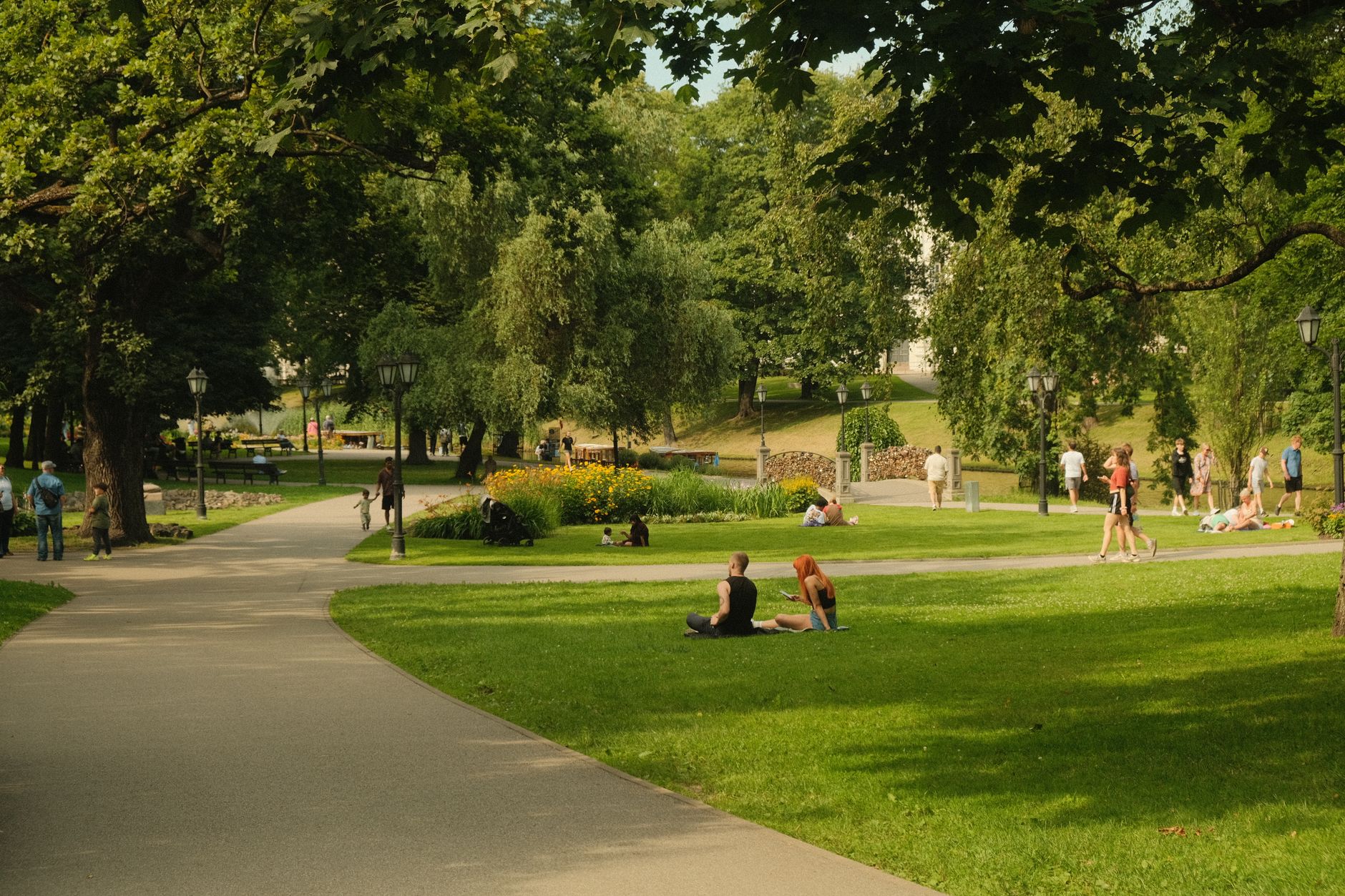 People relaxing on green lawns and walking park paths on a sunny summer day