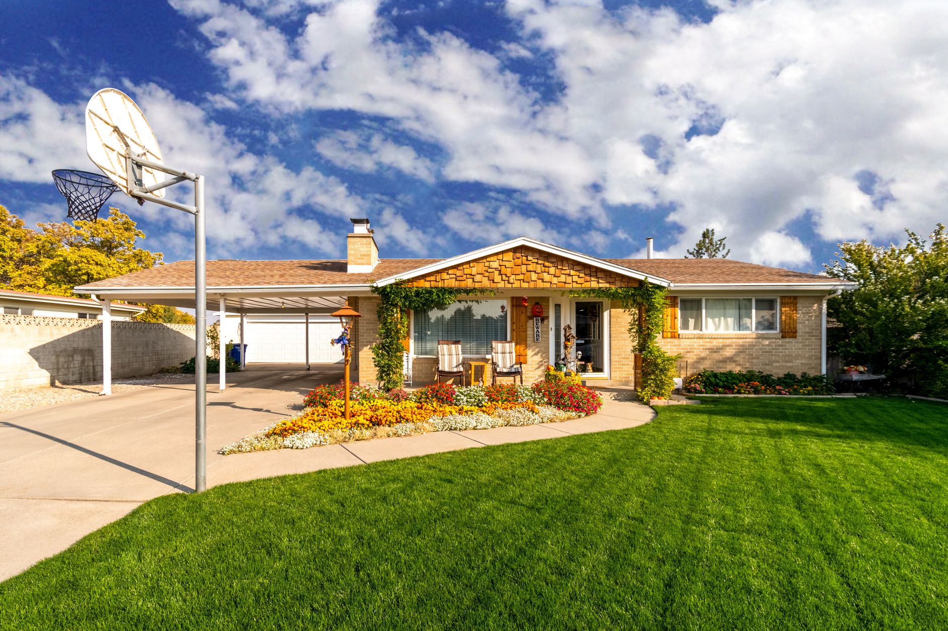 A suburban brick house with a tidy green lawn and a bed of yellow and orange flowers
