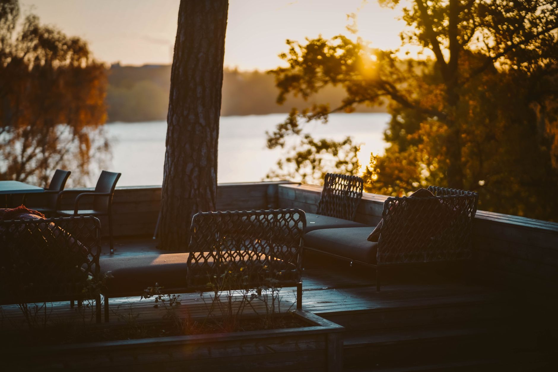 A wooden deck with woven patio furniture overlooking a lake at golden hour