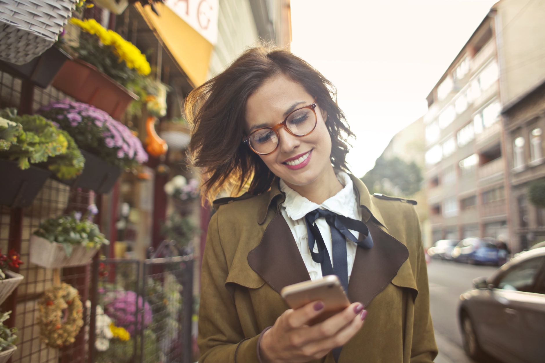 A smiling woman checking her smartphone on the sidewalk outside a flower shop display