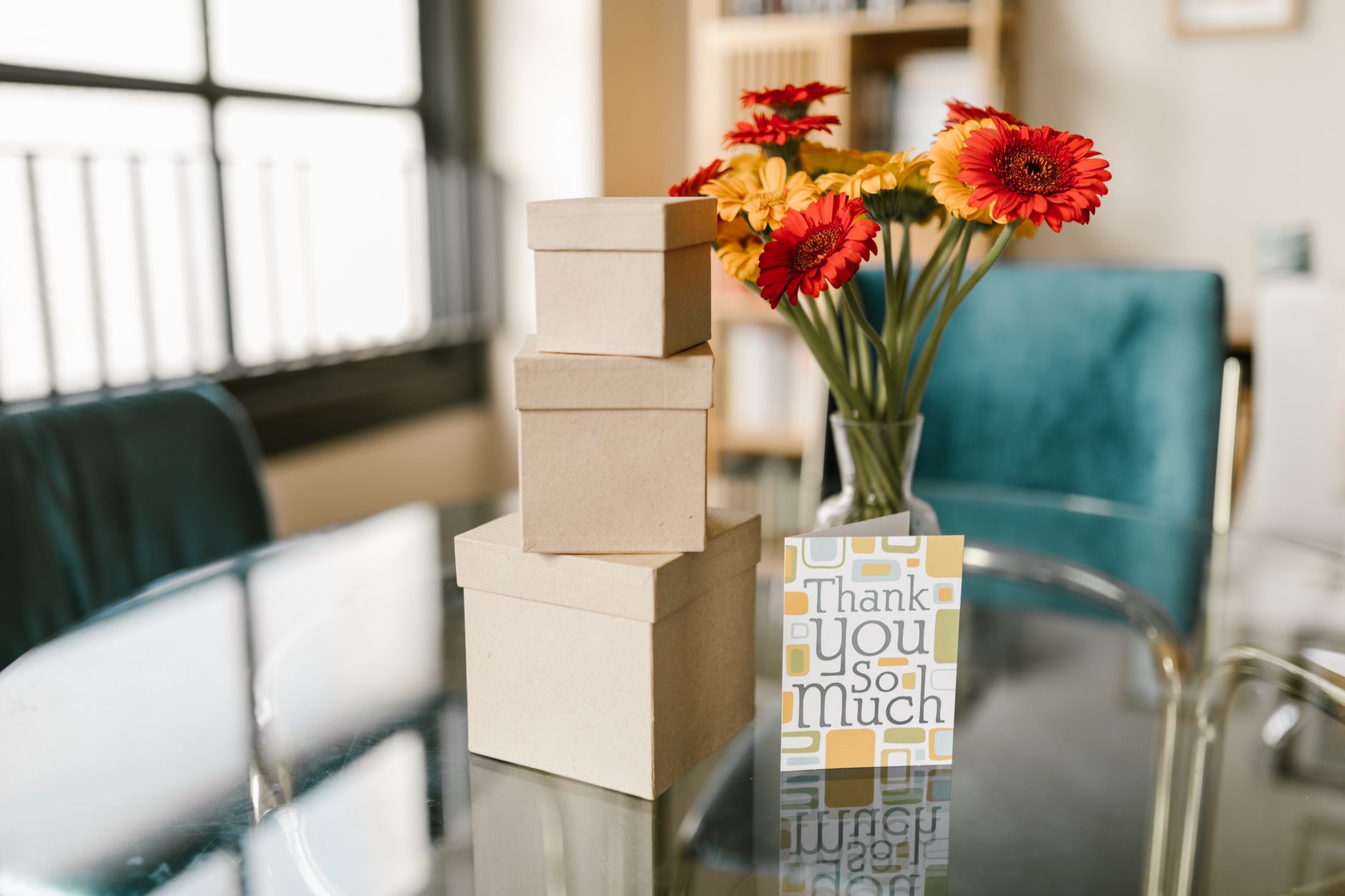 A Thank You So Much card next to gift boxes and orange and yellow gerbera daisies