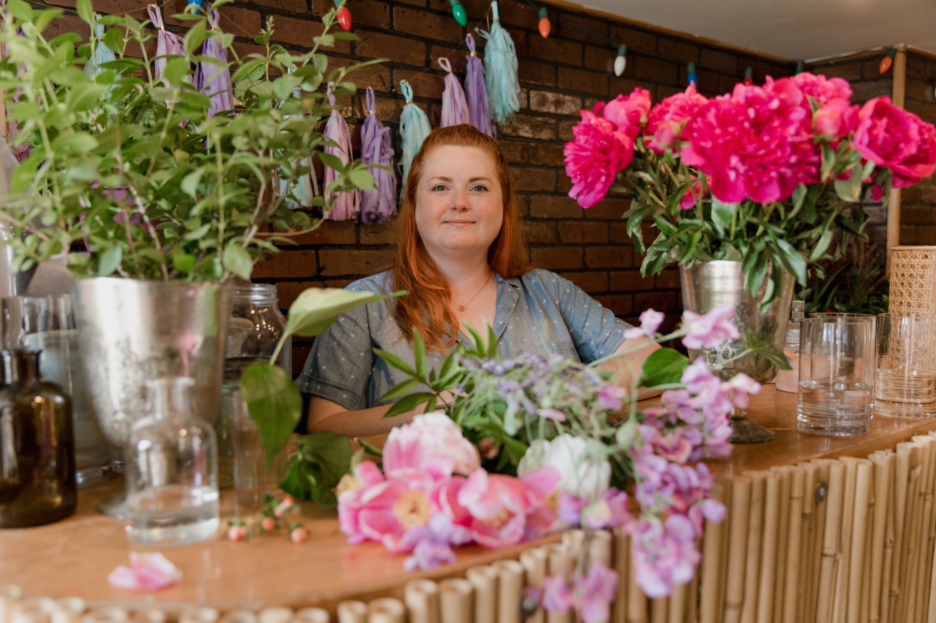 A smiling florist standing behind a counter of fresh flowers in a cozy brick-walled shop