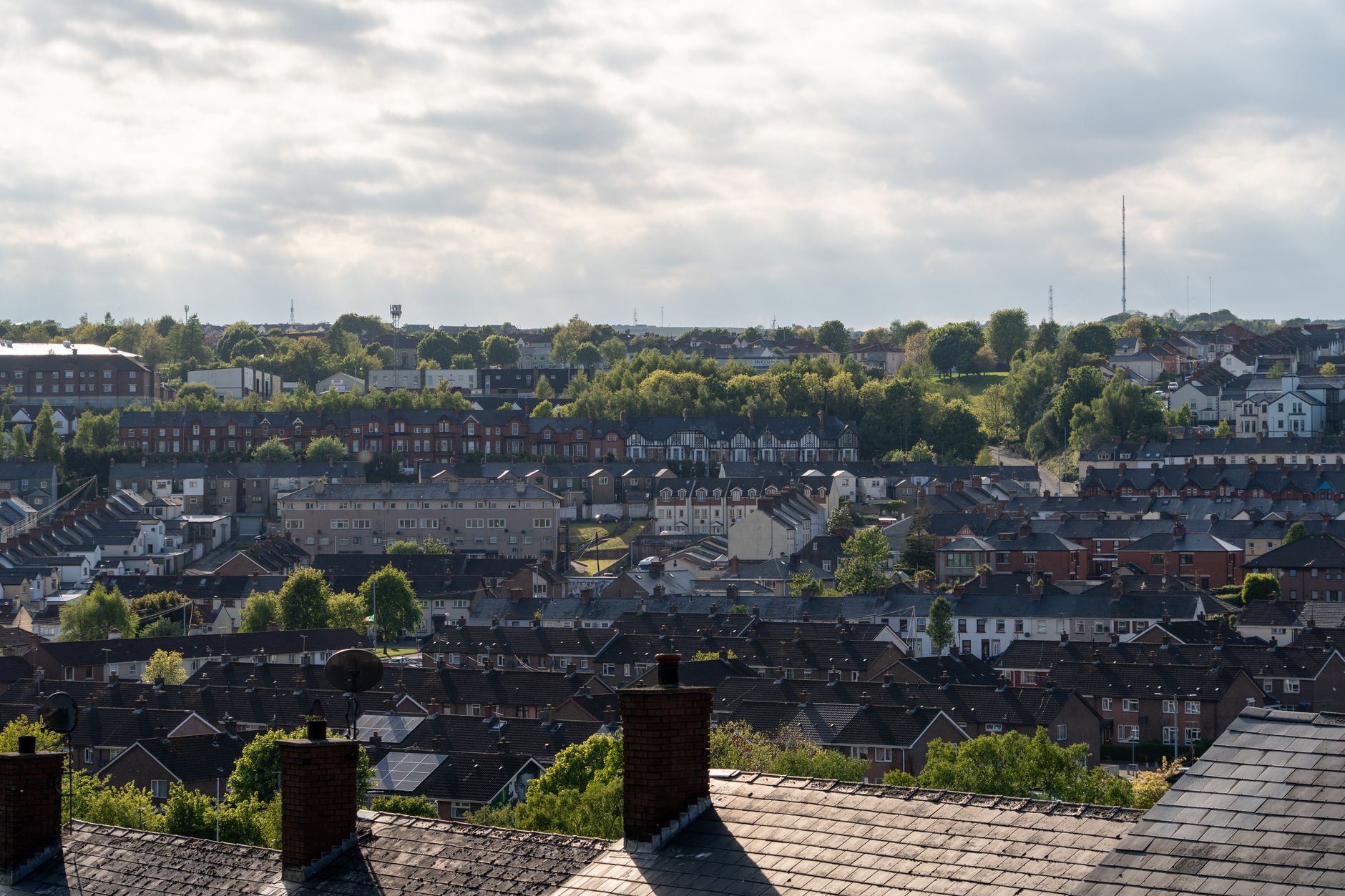 A view over brick rooftops and chimneys of a hillside neighborhood with green trees